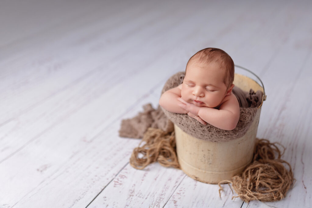 Burlington newborn photography showing a classic bucket pose with a baby boy in soft neutral tones.