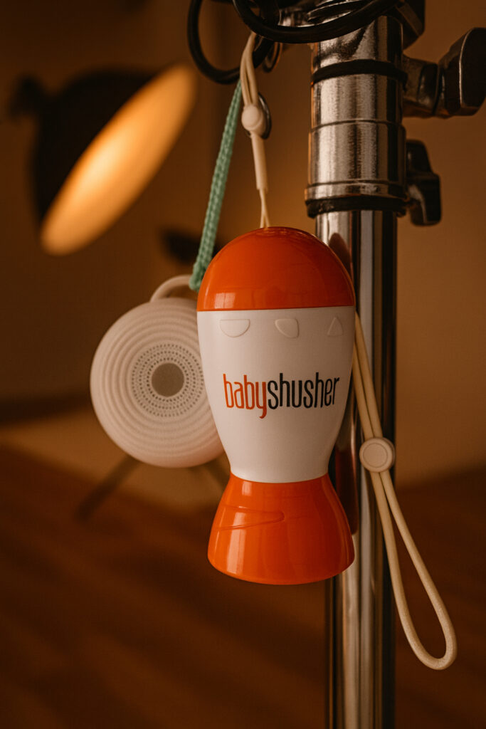 Baby Shusher and Rohm portable sound machines hanging on a studio stand, showing two popular tools used to soothe newborns during photography sessions.