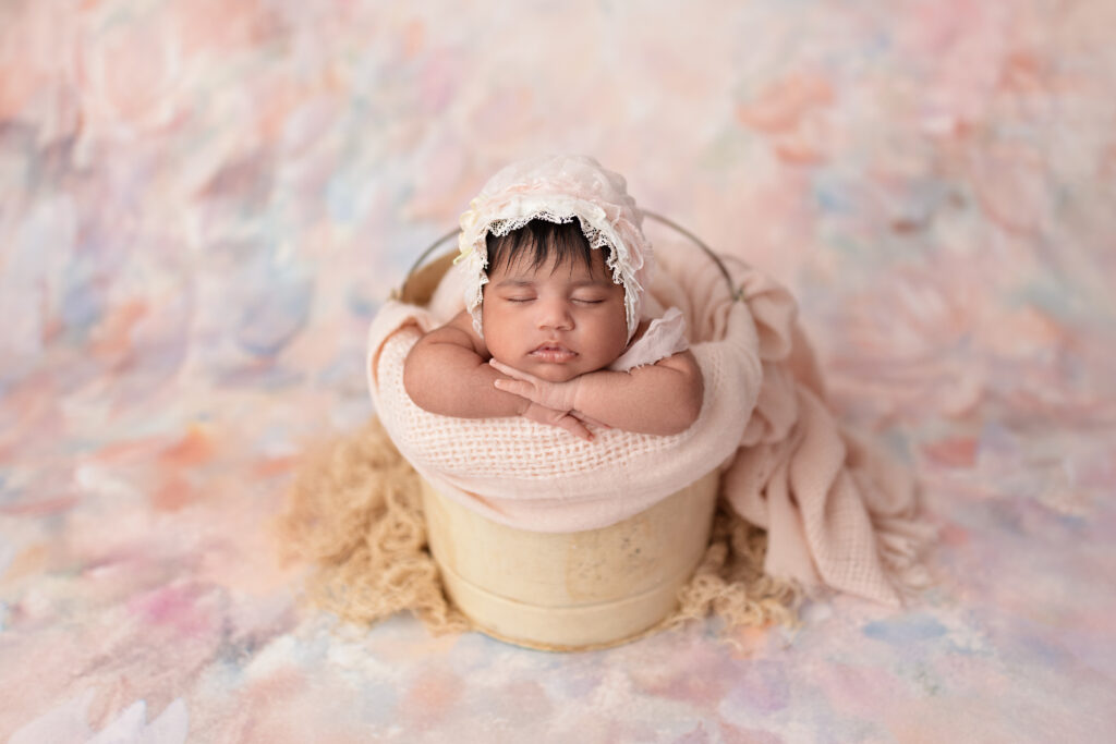 Swaddled newborn in a bucket posed safely in a warm photography studio in Mississauga.