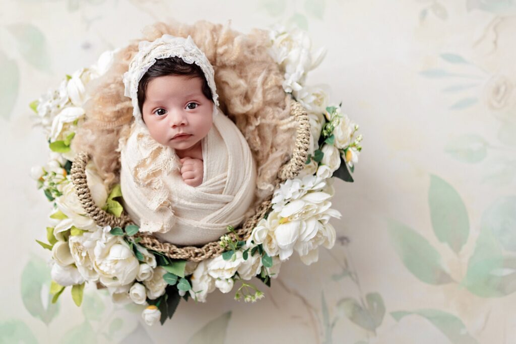 Newborn lies wide awake in cream swaddle in a basket with white flowers at one of the best photography studios in Mississauga. 