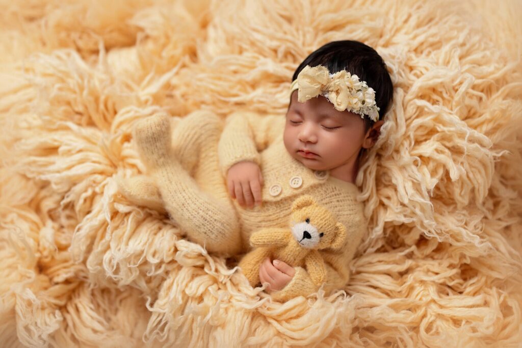Newborn lies in fluffy light orange prop as she snuggles teddy bear at one of the top photography studios in Mississauga. 
