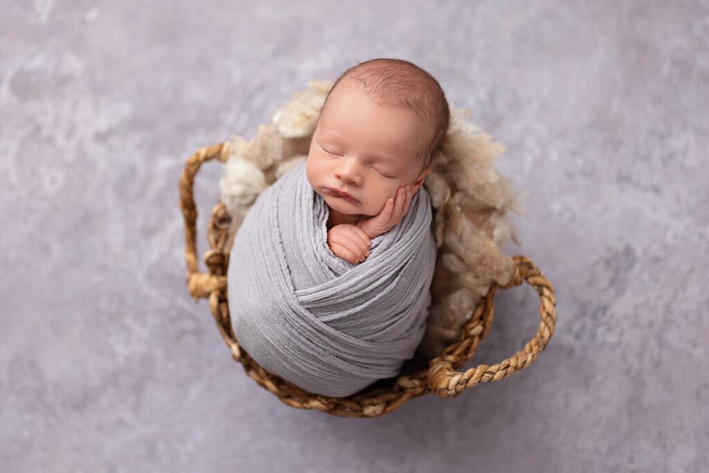 Sleeping newborn wrapped in grey, posed in a woven basket during an Oakville photography session by McLelland Photography