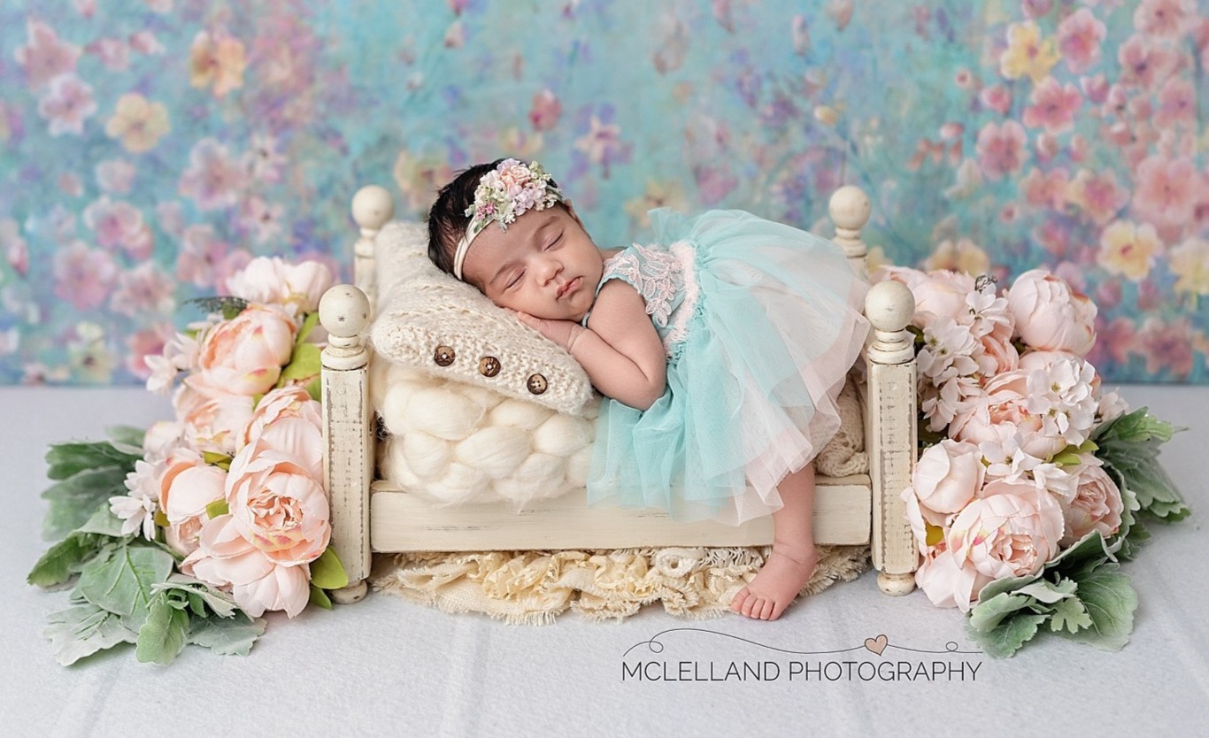 beautiful newborn girl posed safely on a small bed during her newborn photoshoot