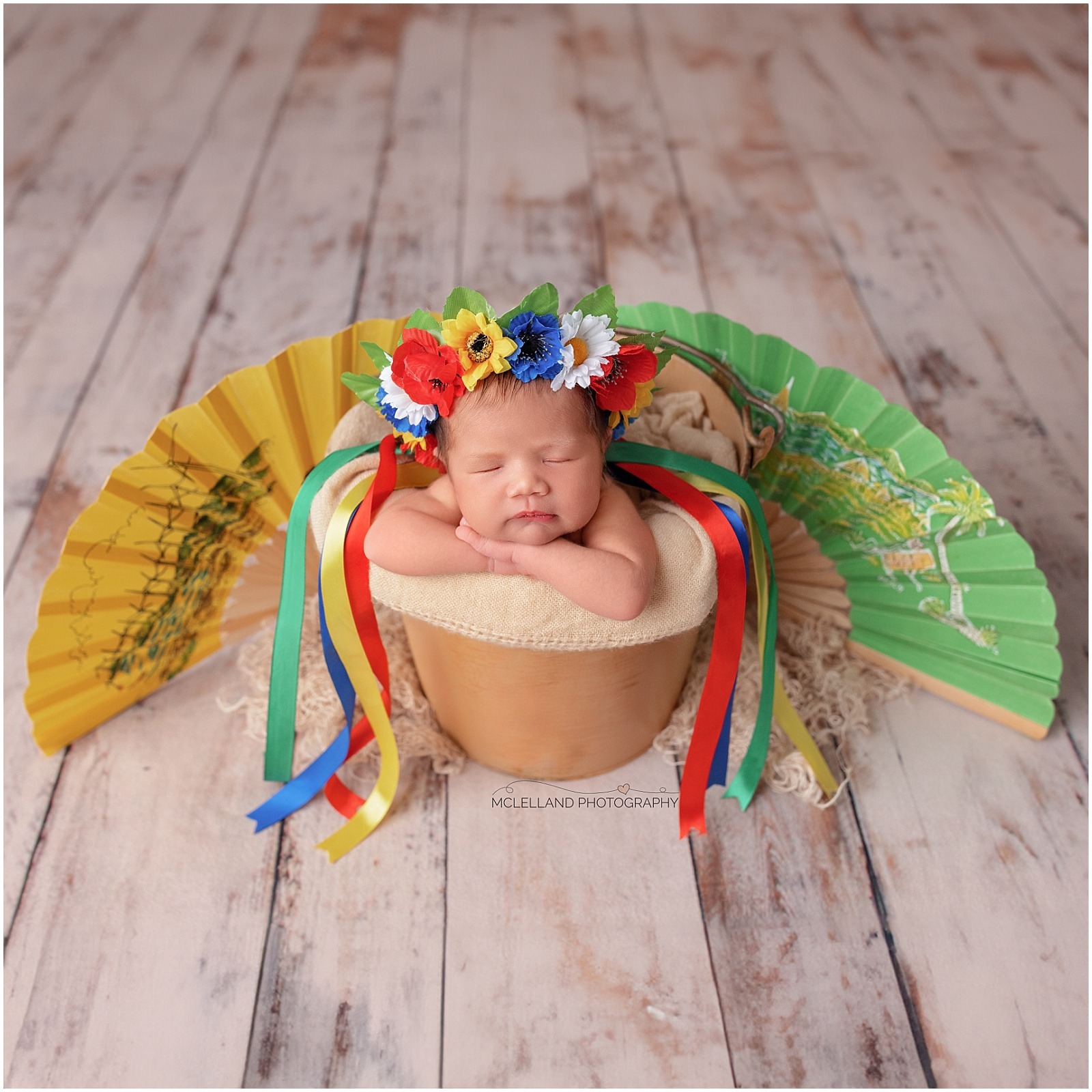 Sleeping newborn baby wearing a colourful flower crown in a professional composite portrait with decorative fans