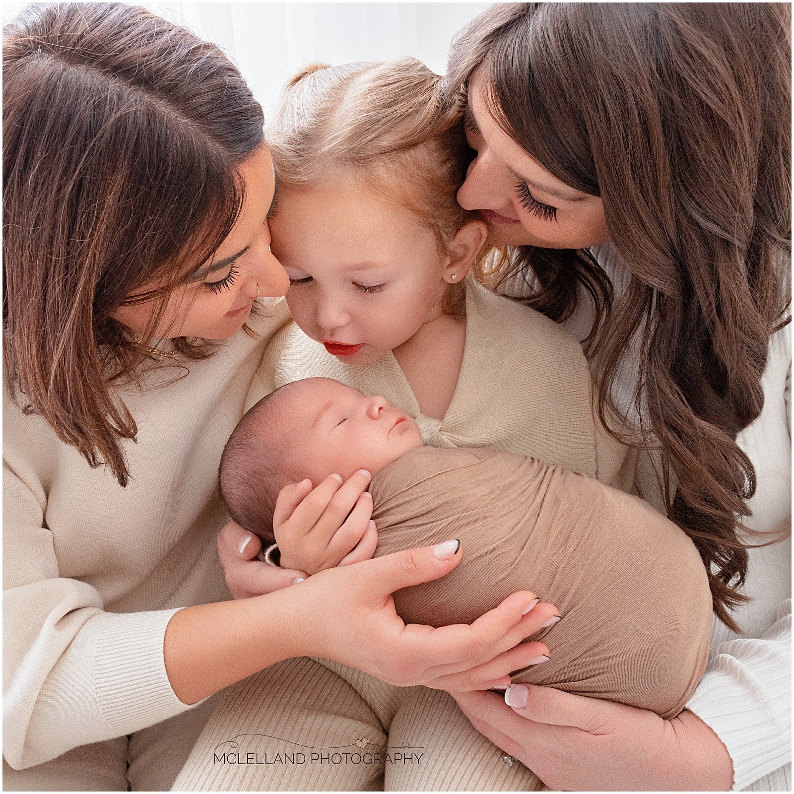 Parents and older sibling gathered around a sleeping newborn baby during a family portrait