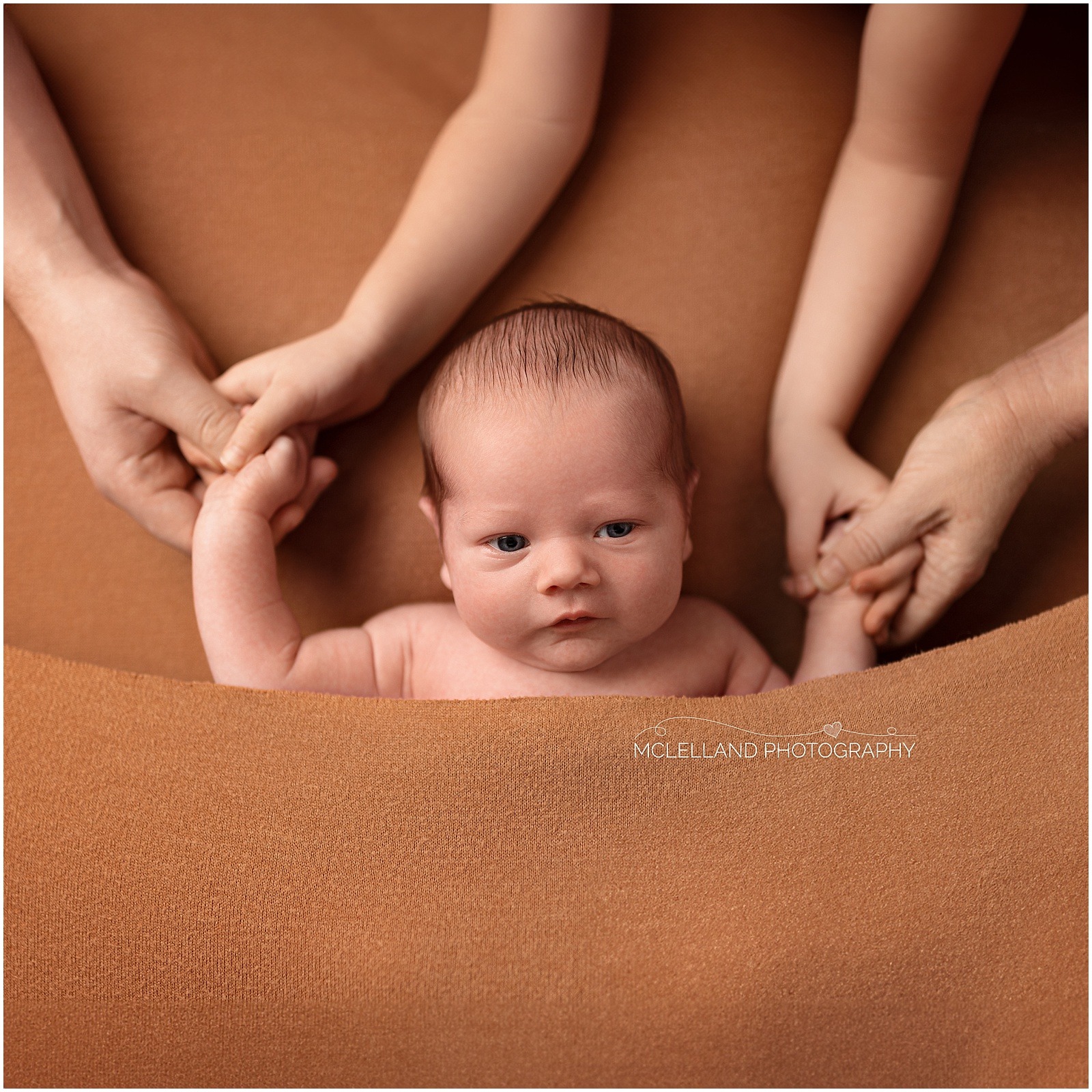 Awake newborn baby holding hands with family members during a close-up portrait