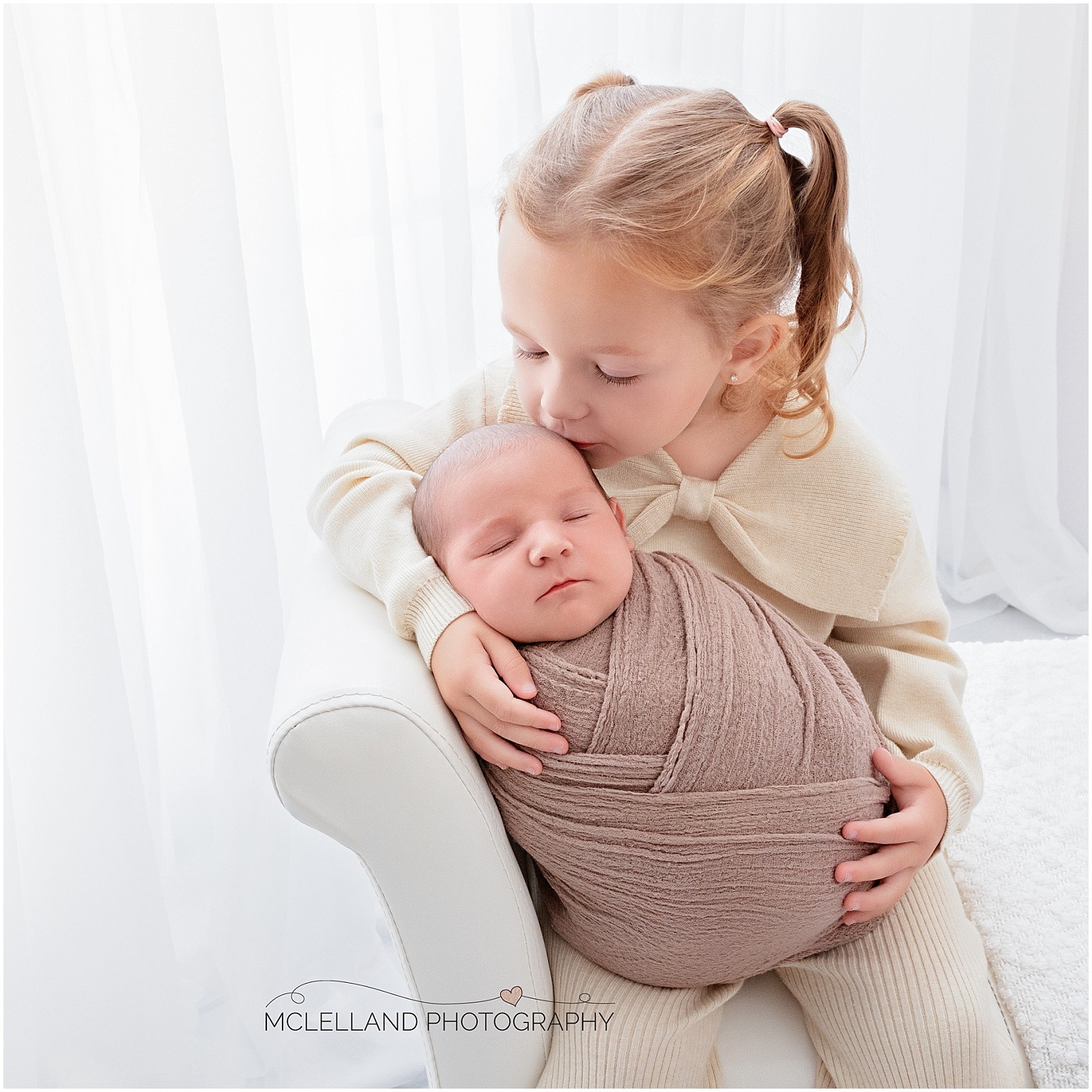 Older sister kissing a sleeping newborn during a newborn photography session with siblings