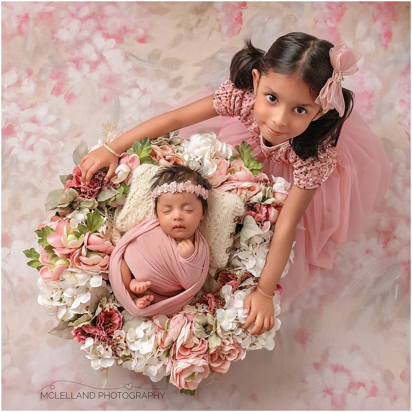 Older sister beside her sleeping newborn sibling in a pink and white floral setup