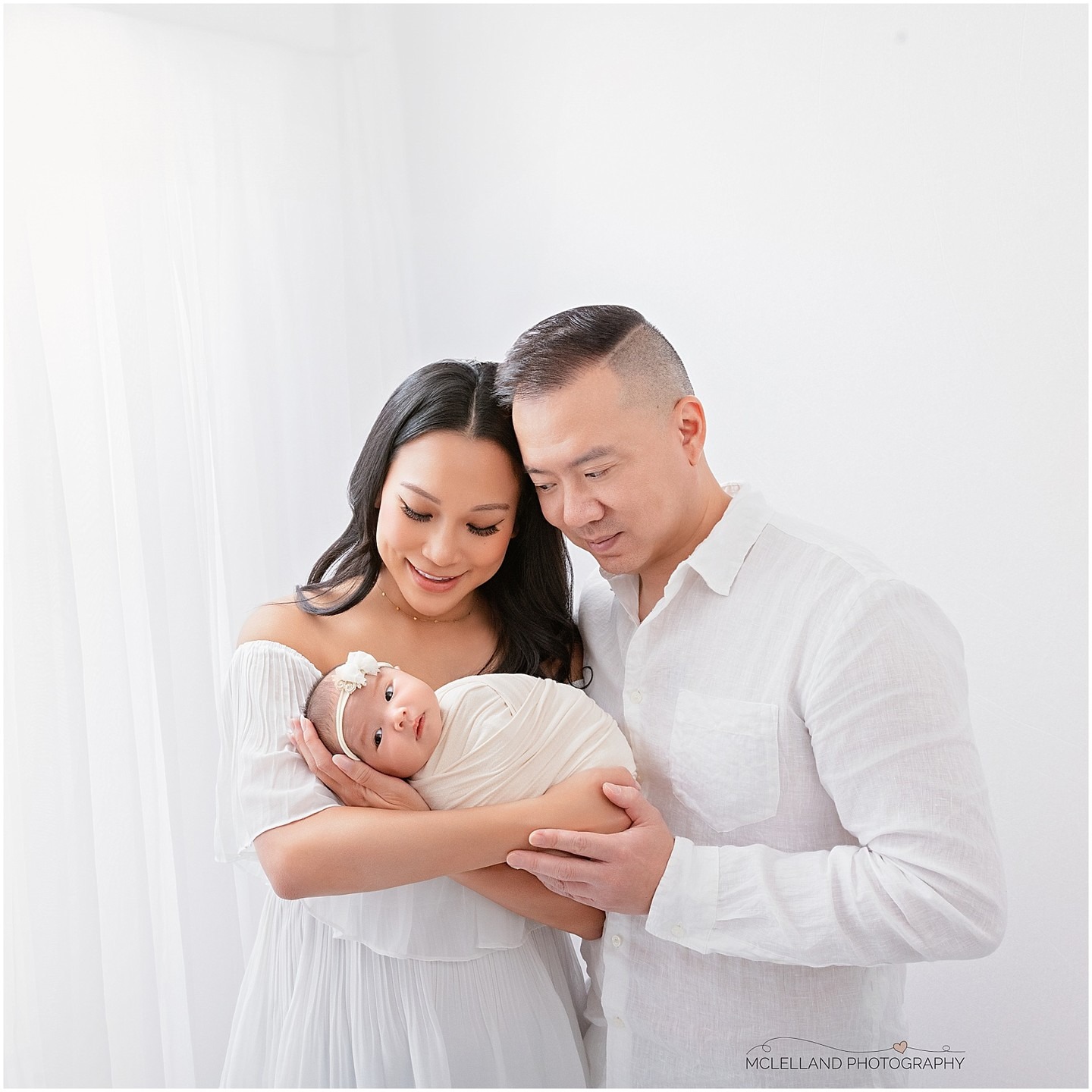 Mother and father looking down at their awake newborn baby while holding her together