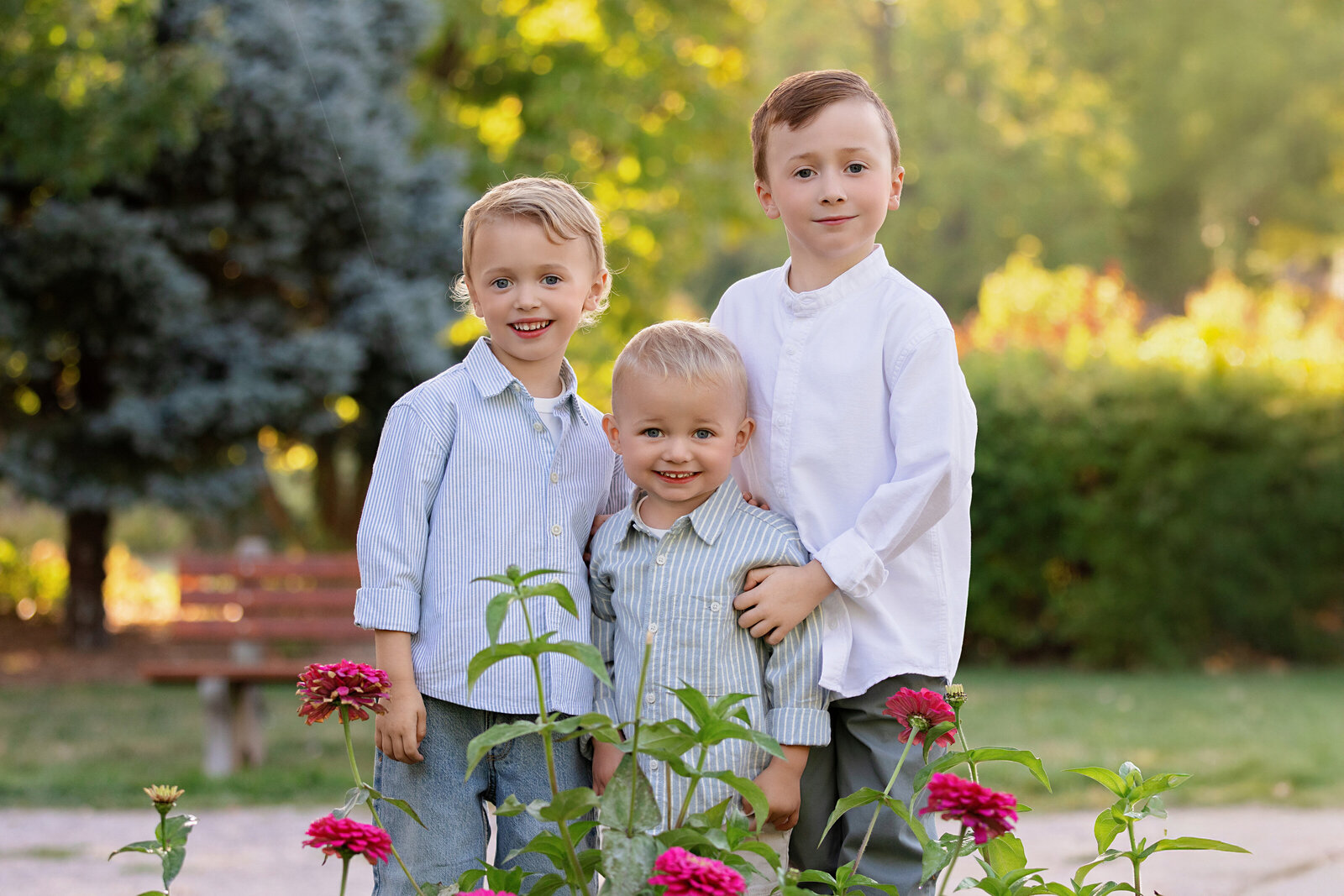 hree young brothers smiling together in a garden with pink flowers during an outdoor sibling photography session
